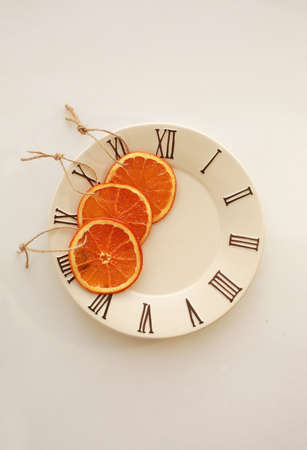 Three dryed orange slices on small plate with clock face icon. Light gray background.の写真素材