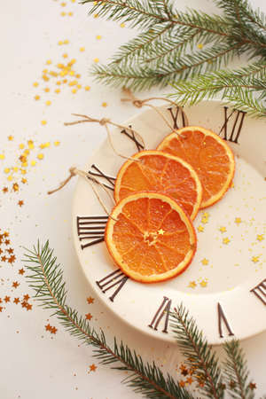 Three dryed orange slices on the plate with clock face icon. Light background with green branch, glitter and golden starsの写真素材