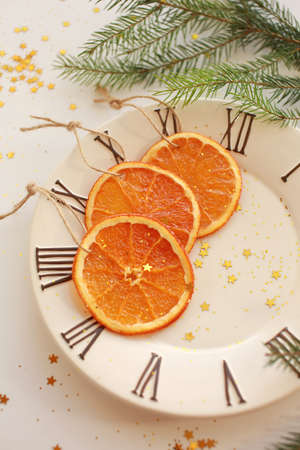 Three dryed orange slices on the plate with clock face icon. Light background with green branch, glitter and golden starsの写真素材