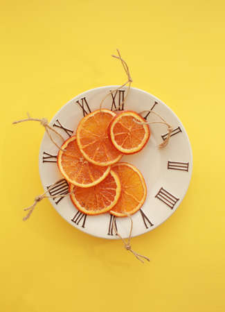 Five dryed orange slices on small plate with clock face icon. Bright yellow background.の写真素材