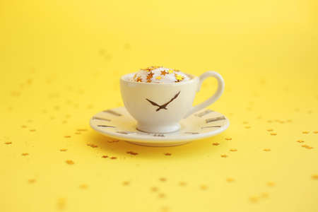 Ceramic white cup with glitter stars inside and small saucer with clock face icon. Yellow background.の写真素材
