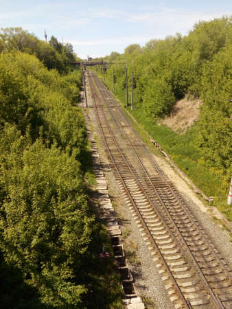 Railroad two branches view from an elevation. Green bushes, a mound of rubble, concrete poles.