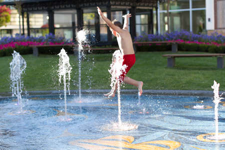 Happy boy running through water in fountain の写真素材