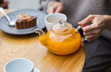 Orange tea and jelly cake on wooden background. A girl pouring sea-buckthorn tea into the white cup. Breakfast in the street cafeの写真素材
