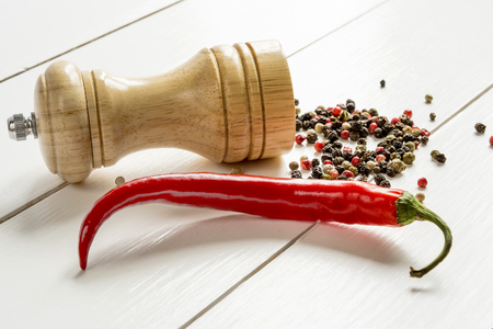 Red hot pepper and pepper mill in the background scattered peas pepper on white wooden tableの写真素材