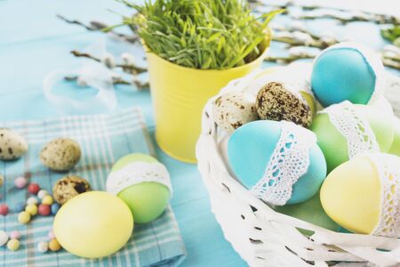 colorful easter eggs in a white wicker basket on blue table against the backdrop of greenery in...