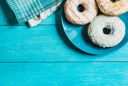 three glazed donuts on blue plate over blue wooden table top viewの写真素材