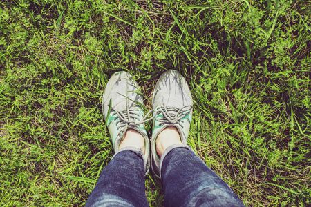 Female legs in gray sneakers and jeans on the grass on a sunny dayの写真素材