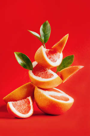 pyramid of grapefruit lobules in a balance decorated with green leaves on a red backgroundの写真素材