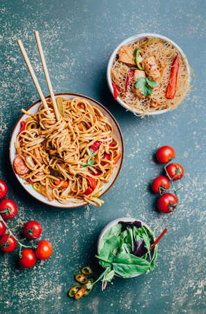close-up of a dish of chinese noodles with meat and vegetables in plates and chinese chopsticks on a green backgroundの写真素材