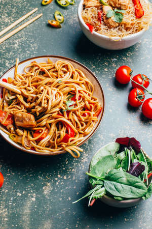 close-up of a dish of chinese noodles with meat and vegetables in plates and chinese chopsticks on a green backgroundの写真素材