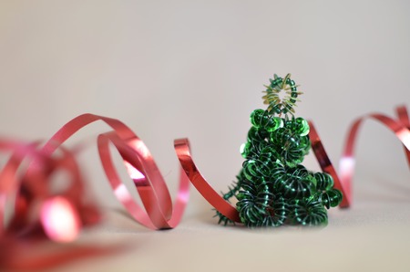 Festive background with a toy Christmas tree from beads and a red wave from a tapeの写真素材