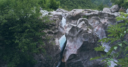 Strong mountain river in rock mountains flows down into white foam waterfall. Beautiful water stream fast flow in mountain landscape. Clear water flows between scenery canyon rocks natureの写真素材