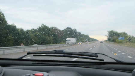 Car windshield during light rain. Car moves by rainy day along the highway, the wind blows off raindrops from front glass of carの写真素材