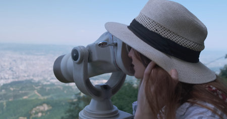 Woman traveler looking at city view, close-up. Beautiful woman in hat, on observation watching through telescope at city Tirana panorama. Mountain Dajti, Albaniaの写真素材