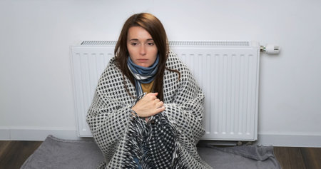Woman cold in apartment. Beautiful woman freezing in warm blanket sitting near central heating...