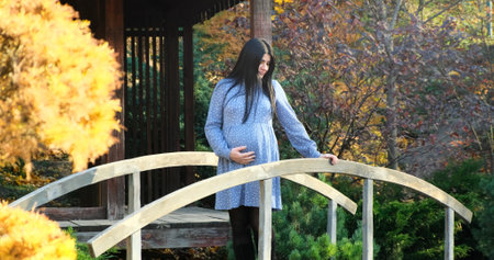 Beautiful pregnant woman walks in autumn park. Happy, pregnant, smiling mother in dress enjoys nature beauty. Maternity happiness outdoor. Expecting baby. Healthy, active pregnancy. Motherhood joyの写真素材
