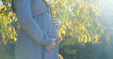 Pregnant woman belly in sun light, close up. Unrecognizable young mother feeling happy on nature background taking care of pregnant belly. Expecting baby, child. Pregnancy, maternity prenatal conceptの写真素材
