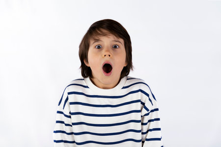 Closeup portrait of shocked scary surprised young boy of nine years old, eyes and mouth wide open, shouting, isolated on white background. Strong emotion facial expression feeling.の写真素材