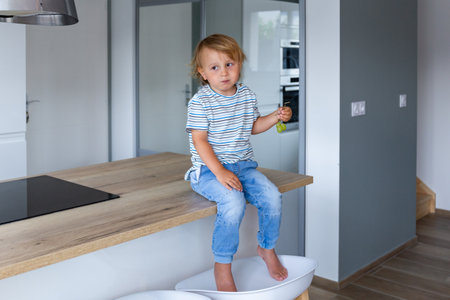 Little boy is sitting on a table in the kitchen and eating grapes. Child is tasting healthy food.の写真素材