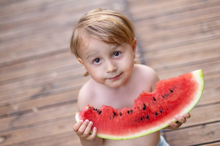 Child eating watermelon in the garden during summer vacances. Kids eat fruit outdoors. Healthy snack for children. Little boy tasting a slice of water melon.の写真素材