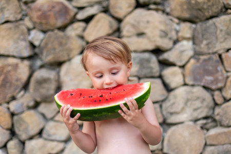 Child eating watermelon in the garden during summer vacances. Kids eat fruit outdoors. Healthy snack for children. Little boy playing in the garden tasting a slice of water melon.の写真素材