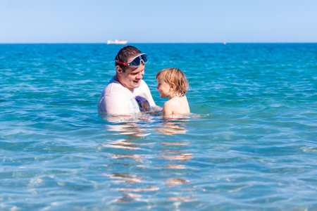 Father and little son having fun swimming and playing together in sea water at summer holidays. Family bonding, togetherness. Seaside vacation.の写真素材