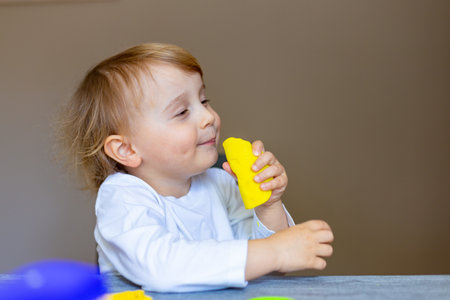 Cute little boy molds from colored plasticine on table. Creative leisure with children during ...