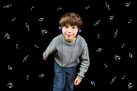 Young boy listening to music on the player with headphones on black background. Music lover. Child excited by song.の写真素材
