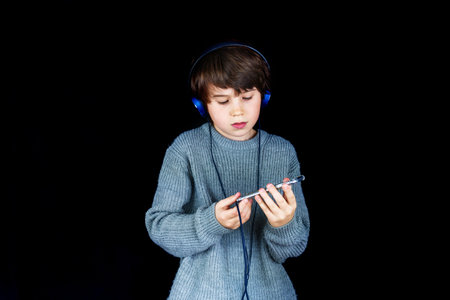 Young boy listening to music on the player with headphones on black background. Music lover. Child excited by song.の写真素材