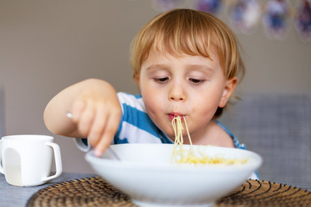 Young boy eating italian pasta at home. Little child enjoying spaghetti meal indoors. Cute kid and healthy foodの写真素材