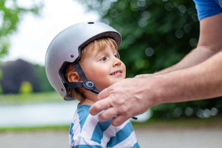 Father puts a safety helmet on little smiling boy for scooter, cycling and rollerblading in the park. child safety on the playgroundの写真素材