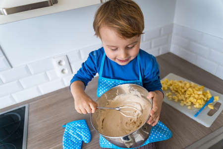 Adorable little boy helping and baking apple pie in home''s kitchen, indoor. Child wearing apron and...