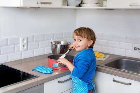 Adorable little boy helping and baking apple pie in home''s kitchen, indoor. Child wearing apron and toque kneading and mixing doughの写真素材