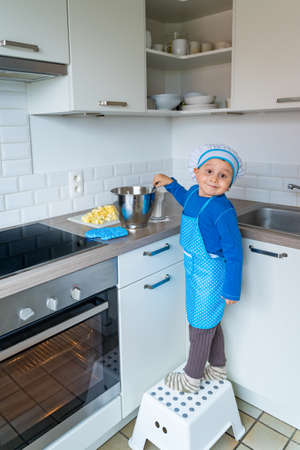 Adorable little boy helping and baking apple pie in home''s kitchen, indoor. Child wearing apron and toque kneading and mixing doughの写真素材