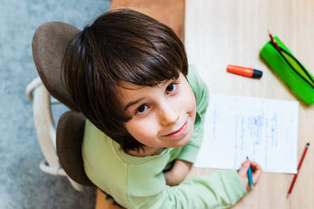 Young school boy doing his homework sitting at the table at home. Concentrated child writing exercises with pleasure. Homeschooliong concept.の写真素材