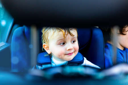 Cute adorable smiling little boy is sitting in the car in safety seat. Children fastening by seat belts travel by car in safety chair.の写真素材