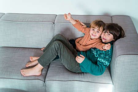 Two brothers lying on the couch at home, smiling and hugging. Good tender relationships between...