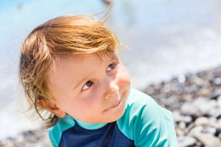 Close up portrait of a little boy of two years old wearing a sun protective t-shirt sitting at the...