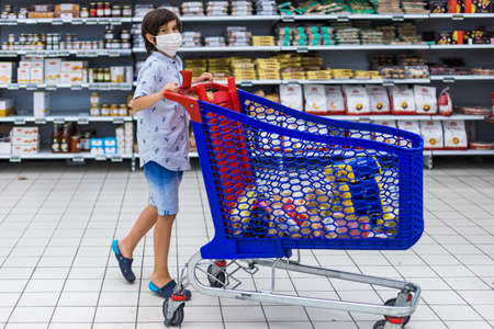 Brussels, Belgium - July 31, 2020: a young boy holding shopping grocery cart with food in a hypermarker Cora Woluwe. Child wearing protection mask during outbreak.のeditorial素材