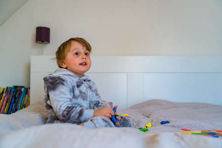 Little toddler boy plays on the bed in a wooden magnetic constructor, preschool child learning at...