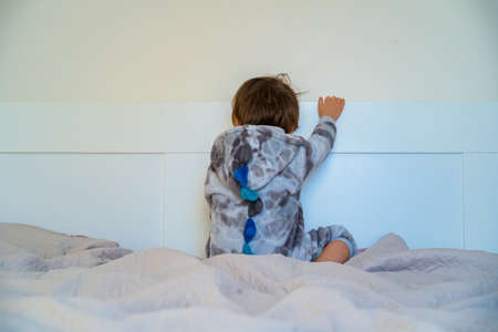 Offended sad child sitting in bed turned away from the camera. Little boy got upset.