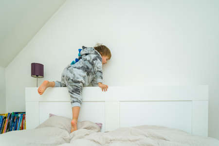 Adorable little boy of three years old playing in bed at home. Child climbing onto the bed and doing gymnastic exercises. Home leisure with children.の写真素材