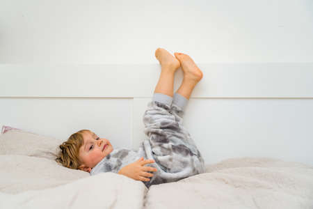 Little toddler boy relaxing on bed. Home leisure. Child playing in bed, lifting legs up.の写真素材