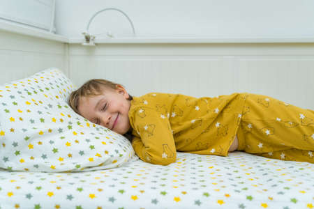 Little toddler boy is lying in bed. Child waking up in the morning with smile. Happy kid resting at home.の写真素材