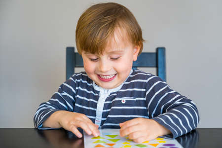 Little boy wearing striped t shirt sitting at the table, learning at home during coronavirus...