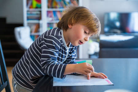 Little boy sitting at the table, learning at home during coronavirus quarantine. Toddler looking at...