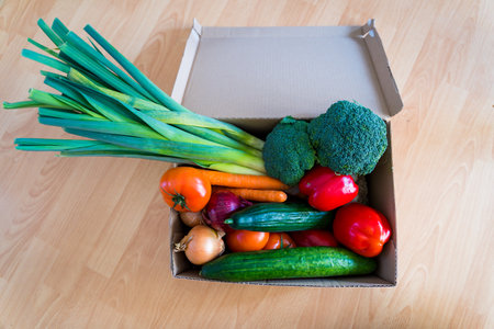 Set of different fresh vegetables in a cardboard box. Home delivery of groceries during  quarantine. Broccoli, leek, cucumbers, bell peppers, tomatos, onions bought in a supermarket.の写真素材