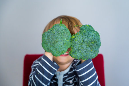 Smiling toddler boy closed his eyes with broccolis. Teaching child to healthy and varied vegitarian food.の写真素材