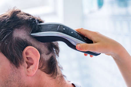 Young boy helping his father to cut hair at home. Son shaving daddy with clipper staying in bathroom during coronavirus quarantine. Hairdressing salons closed.の写真素材